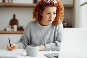A professional woman taking notes while looking at her computer.